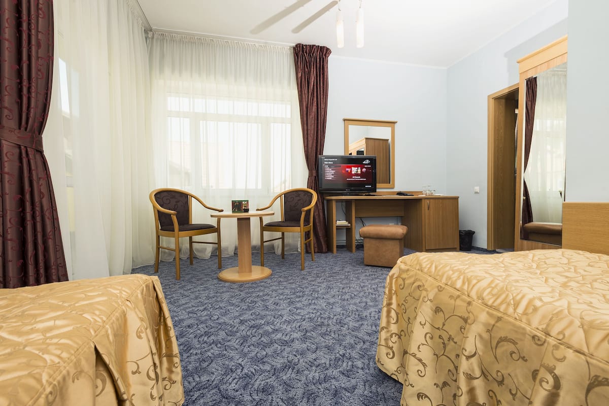 A hotel room with two beds, a desk with a computer, a chair, and a small table.