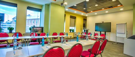 A conference room with red chairs, a long table, a projector, and a whiteboard.