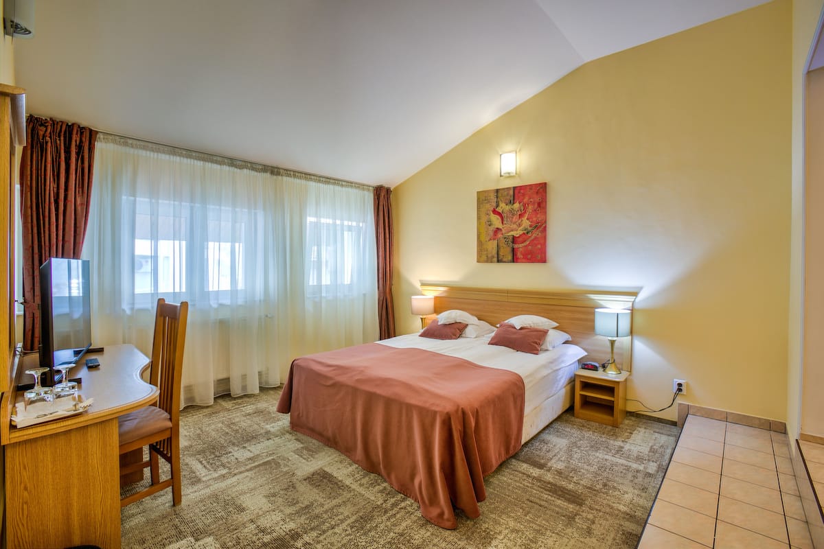 A hotel room with a bed, a desk, a chair, a lamp, and a painting on the wall.