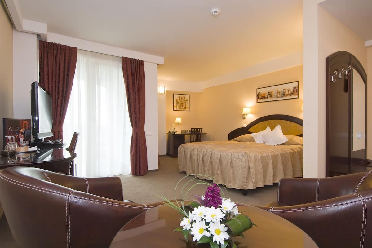 A hotel room with a bed, a desk with a computer, a chair, and a table with a vase of flowers.