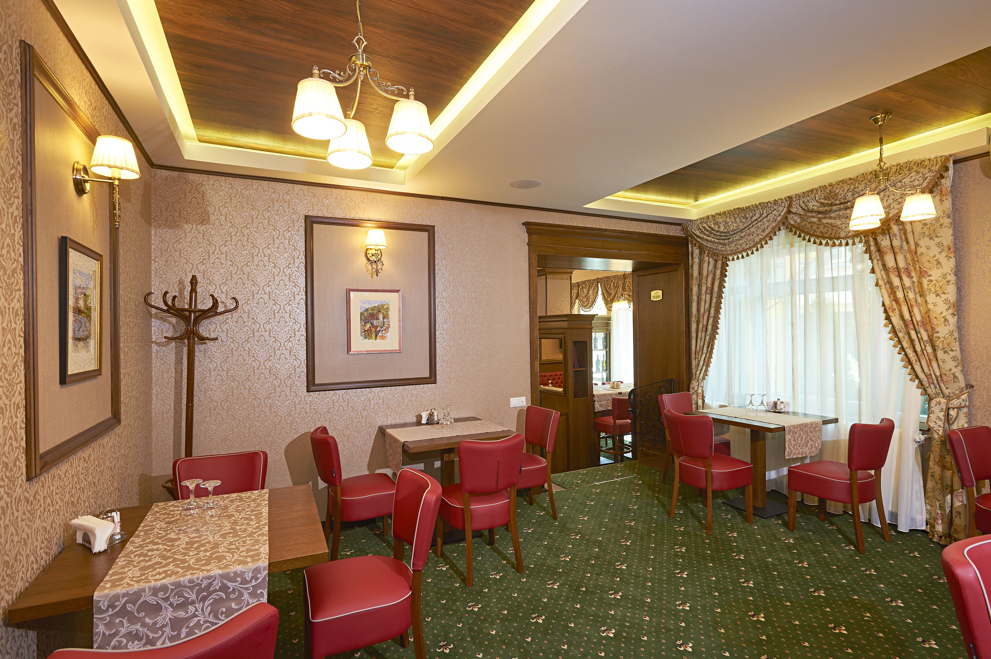 A dining area with red chairs and tables, a chandelier, and patterned wallpaper.
