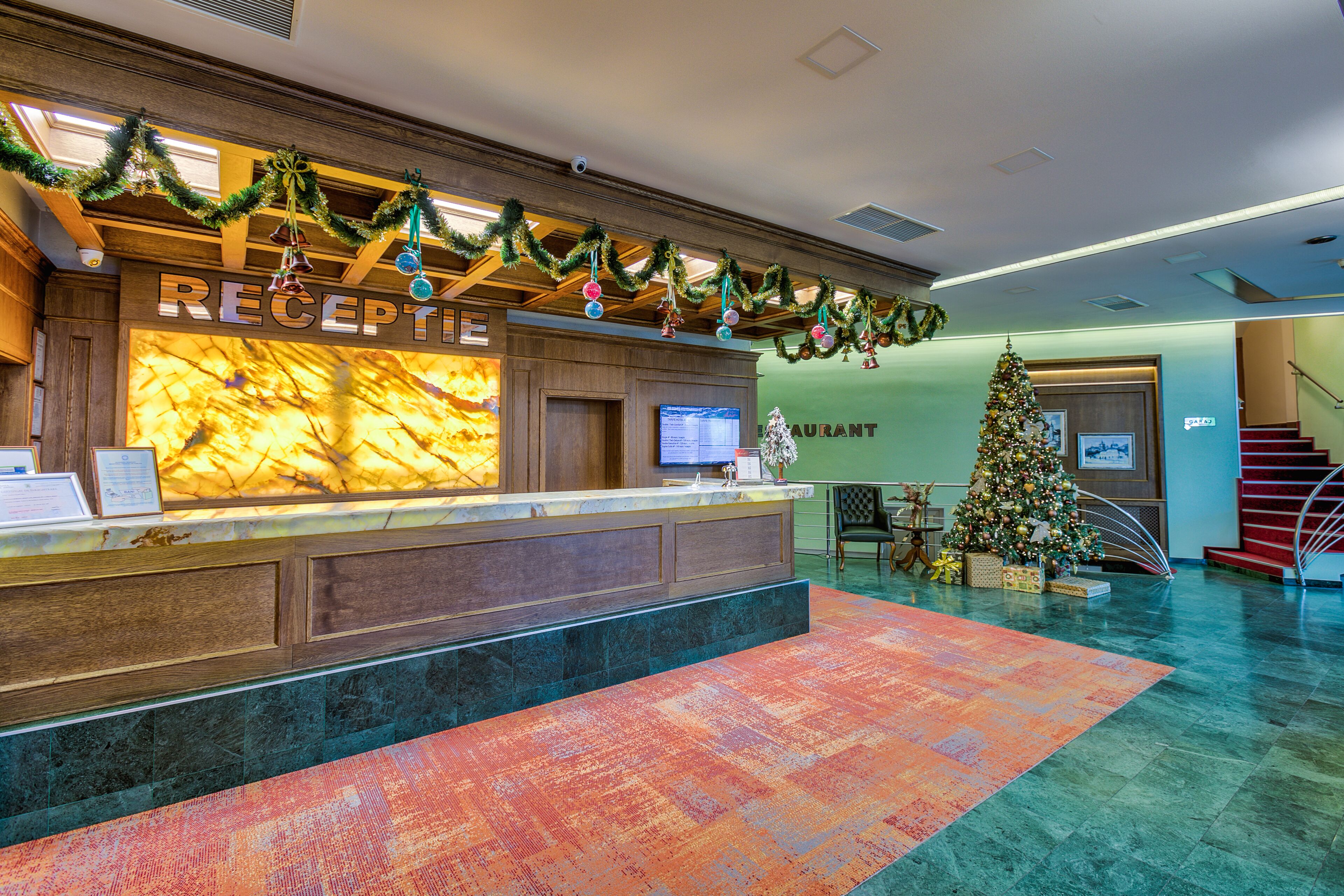 Zona de recepción de un hotel con mostrador de mármol, un árbol de Navidad y una escalera al fondo.