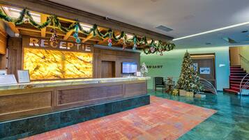 Zona de recepción de un hotel con mostrador de mármol, un árbol de Navidad y una escalera al fondo.