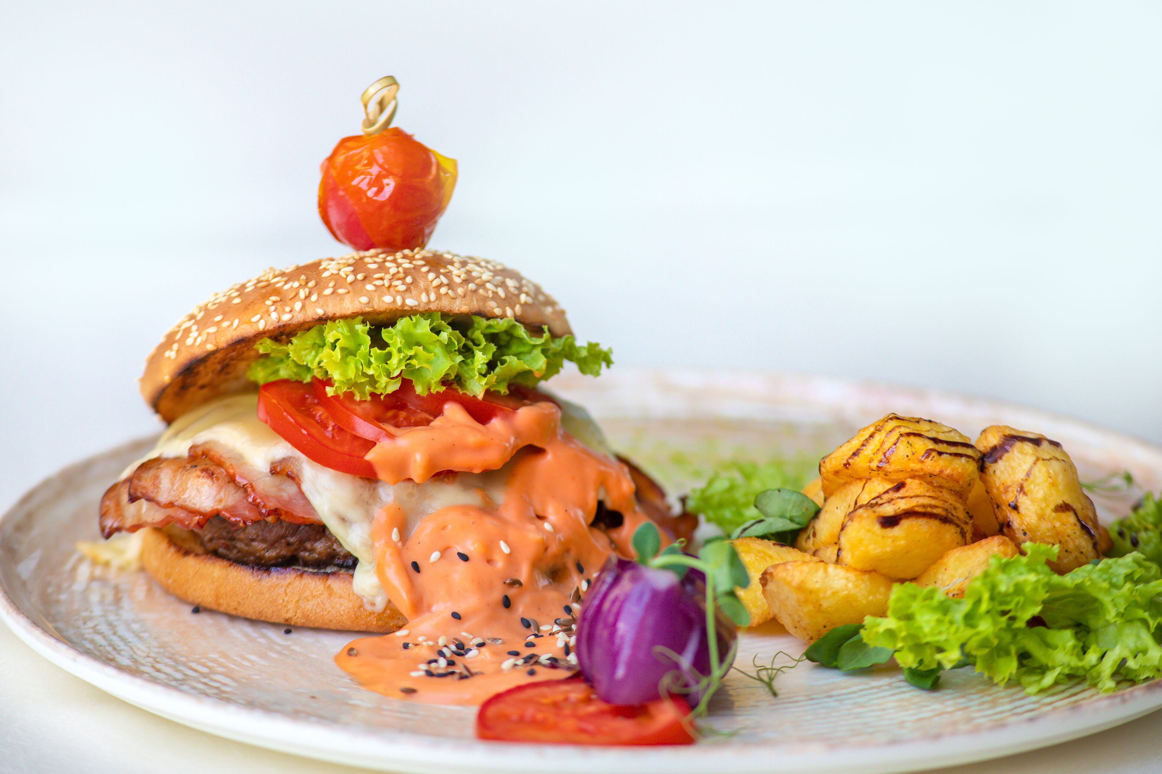 Un piatto con un hamburger, patate grigliate e un pomodoro infilzato su uno spiedino.