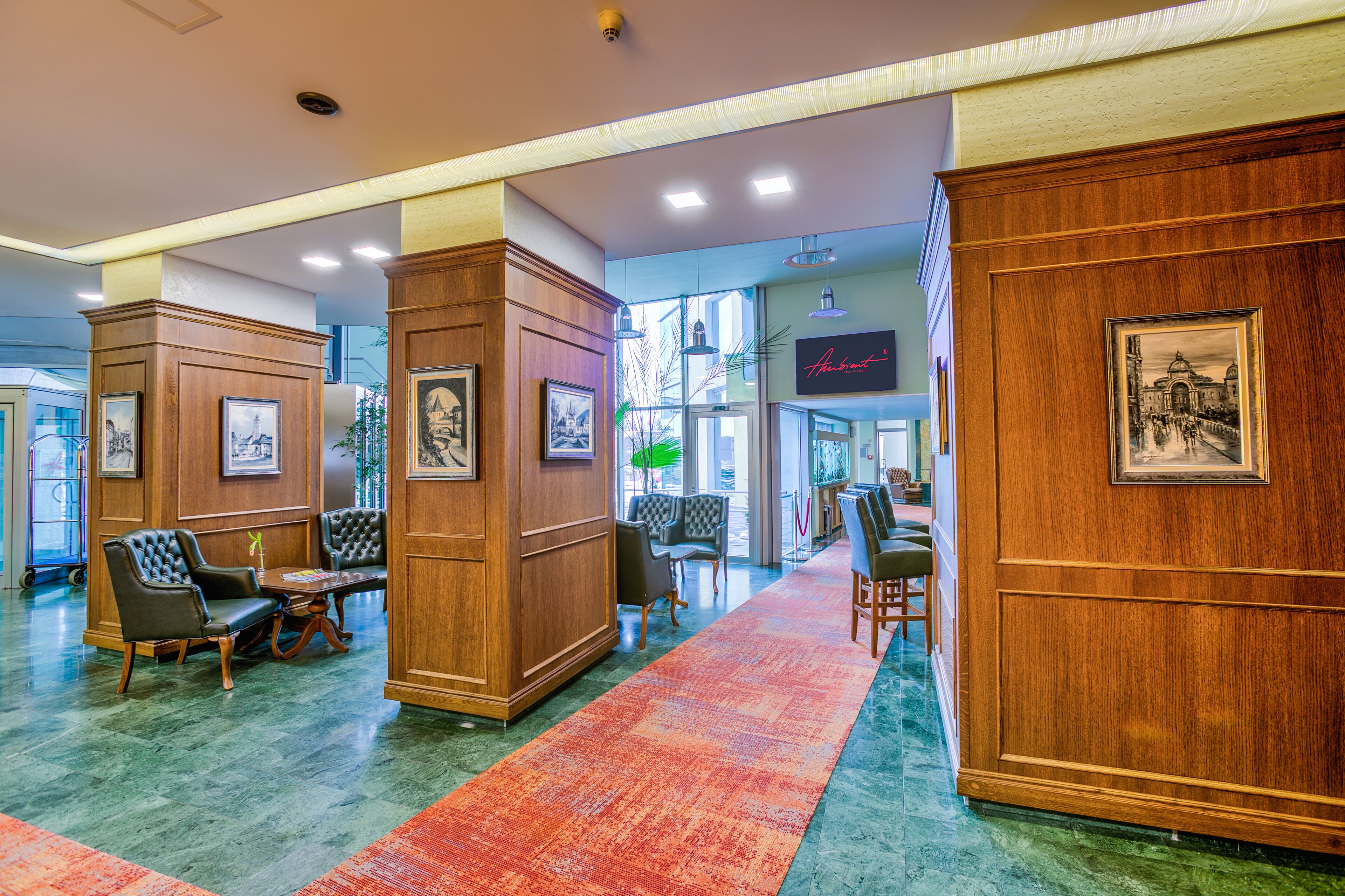 A lobby with wooden paneling, framed artwork, and a red carpet leading to seating areas.