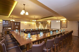 Un salón de conferencias con una larga mesa, sillas, botellas de agua y una pantalla de proyector.