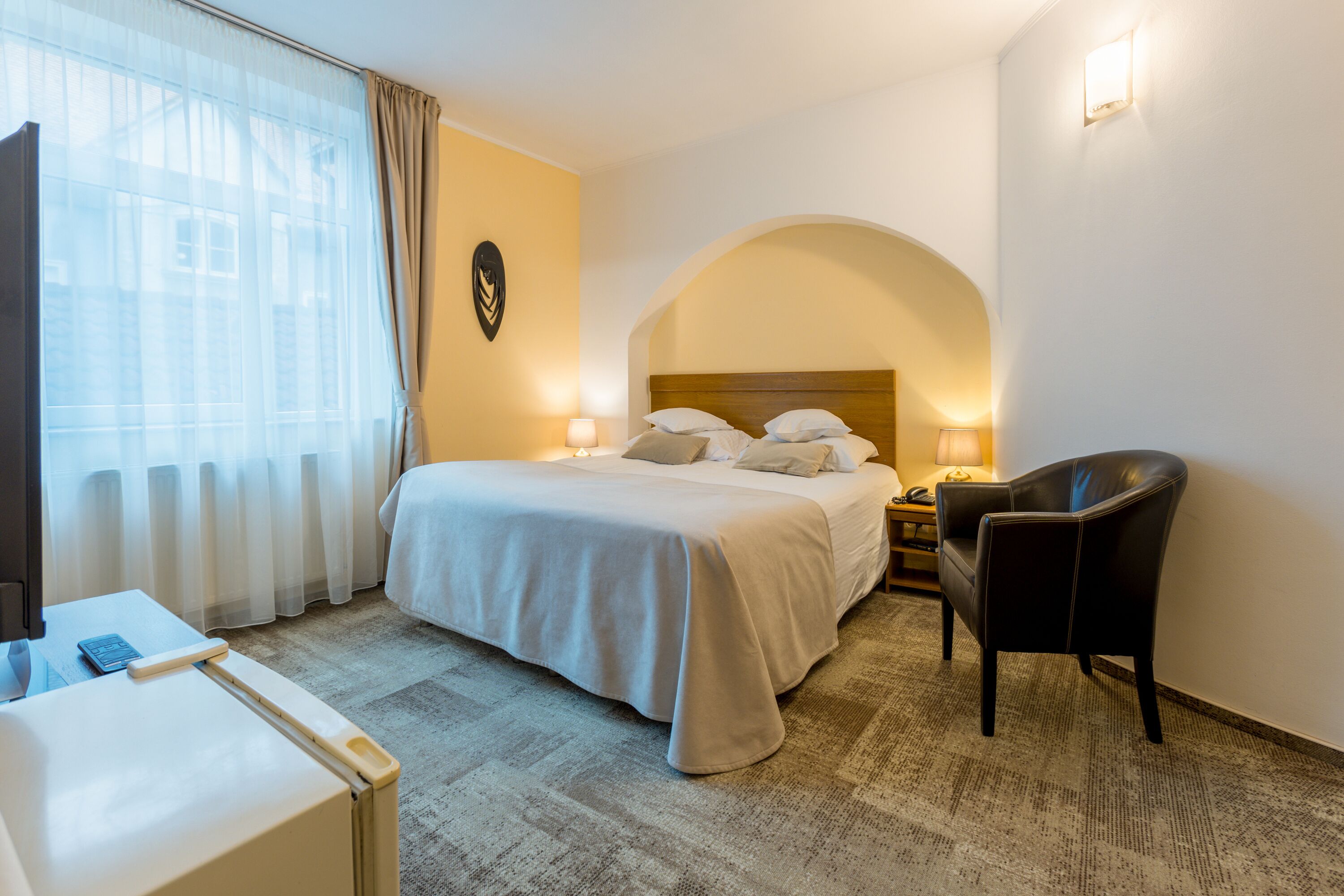 Habitación de hotel con cama, escritorio, silla y un ventanal con cortinas.