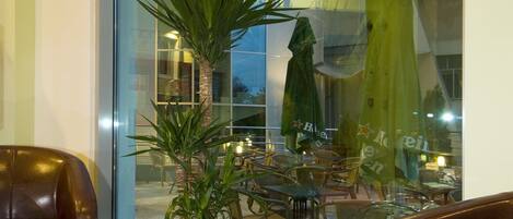 A modern hotel lobby with a glass table, leather chairs, a potted plant, and a view of the outdoor seating area.