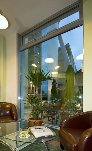 A modern hotel lobby with a glass table, leather chairs, a potted plant, and a view of the outdoor seating area. - Hotel Ambient (Brasov)