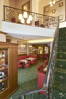 Un vestíbulo de hotel con una escalera, zonas de estar y un bar.