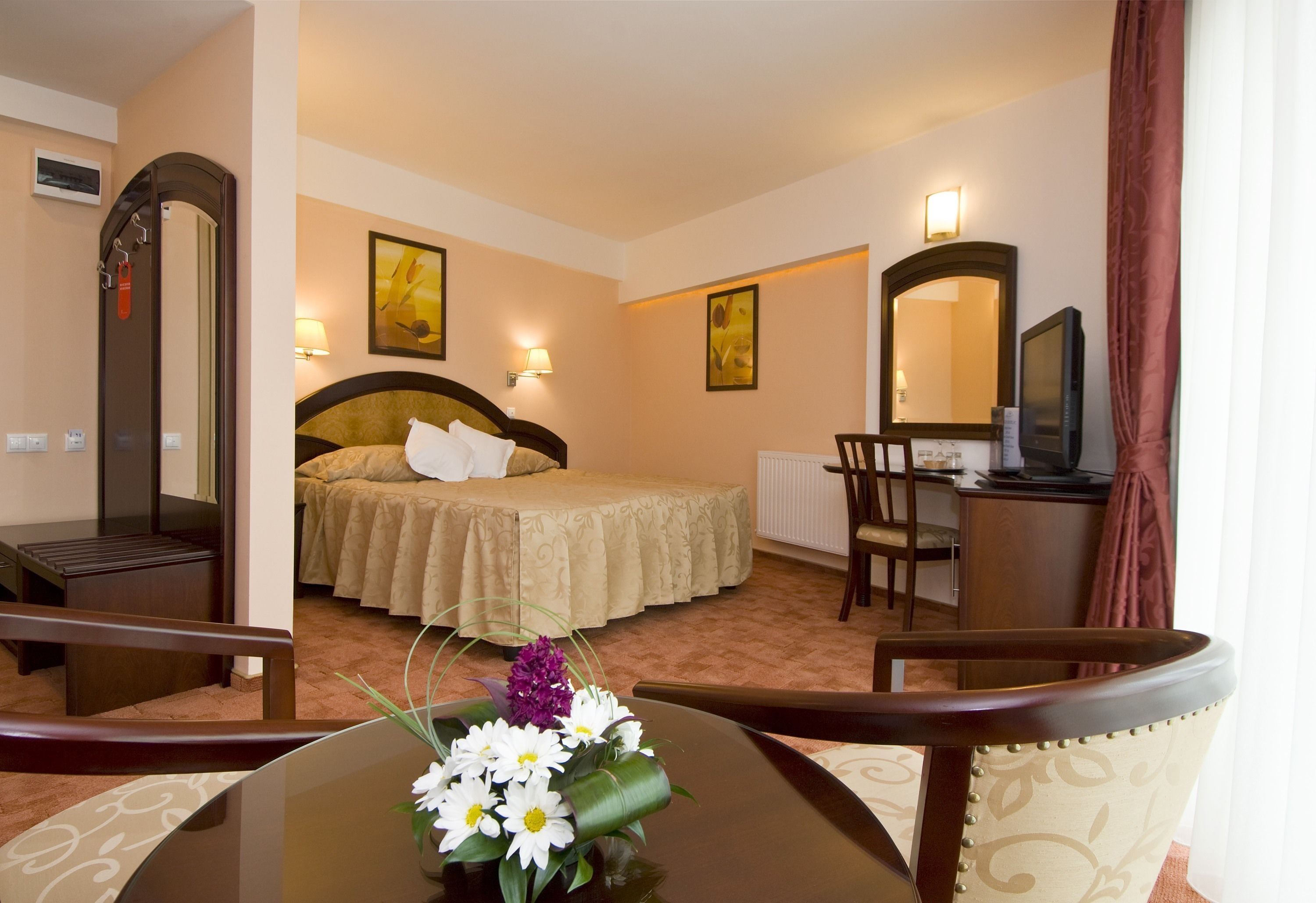 A hotel room with a bed, bedside table, chair, TV, and a mirror.