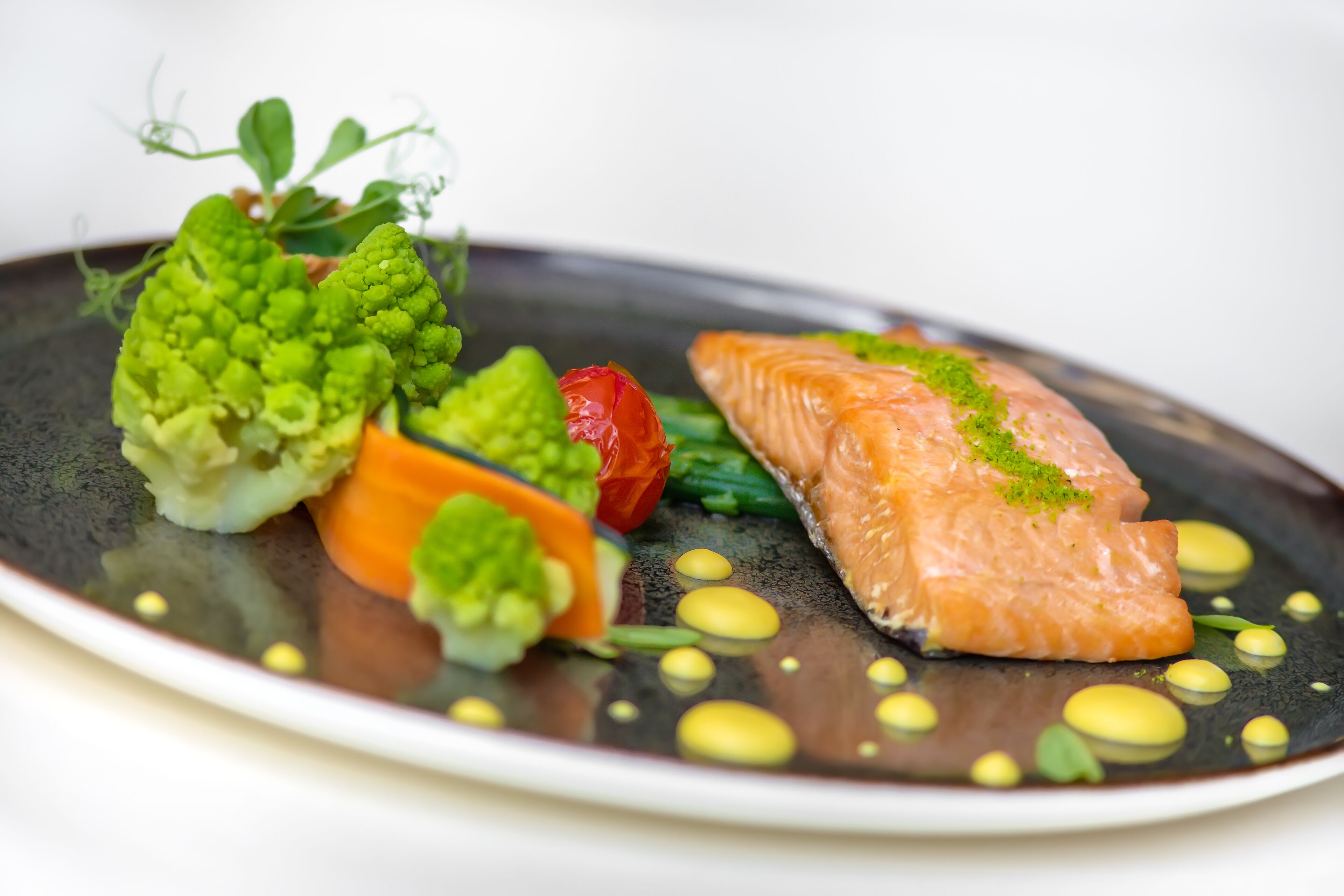 A plate of food with salmon, vegetables, and a decorative garnish.