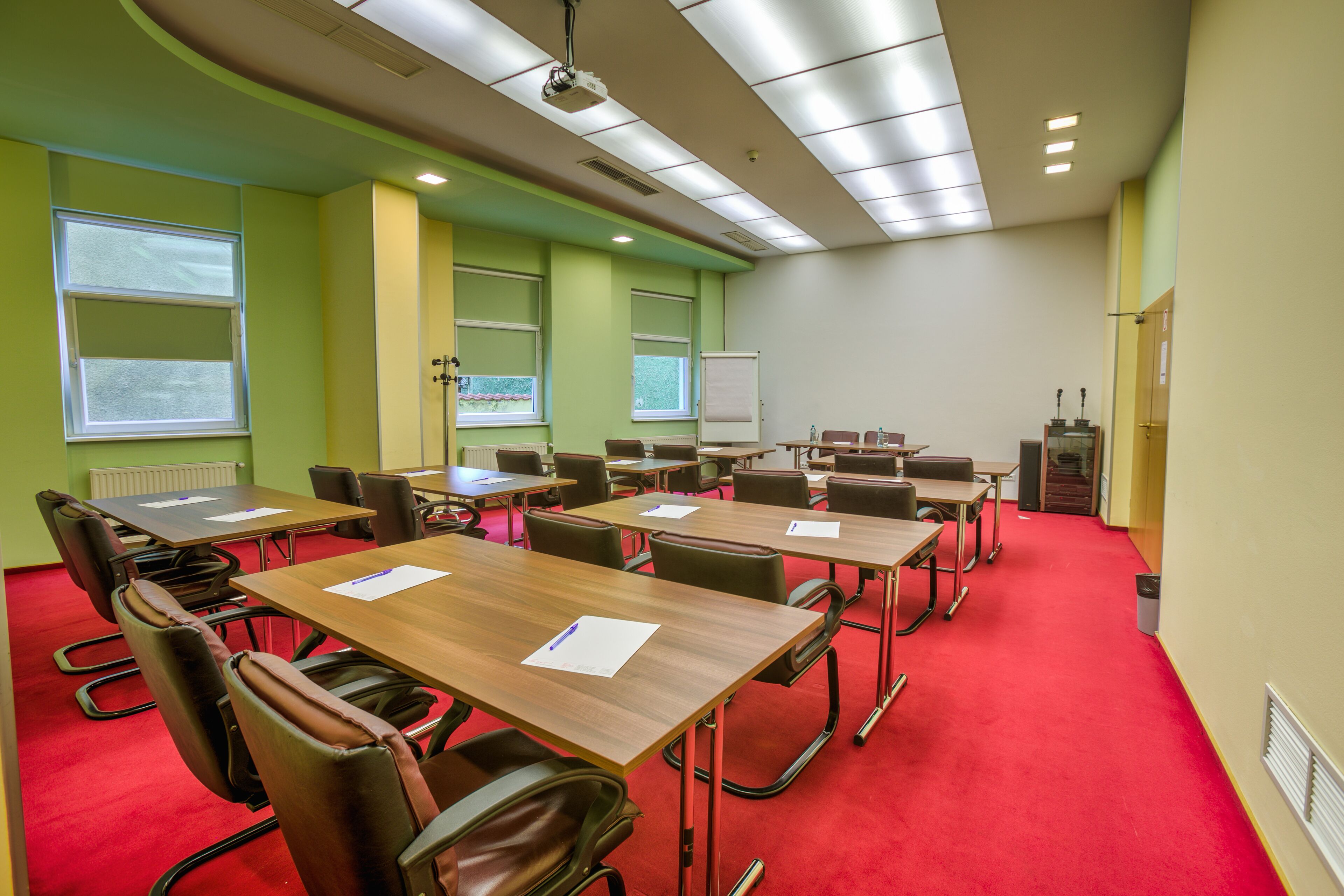 Un salón de conferencias con mesas, sillas, un proyector y una pizarra.