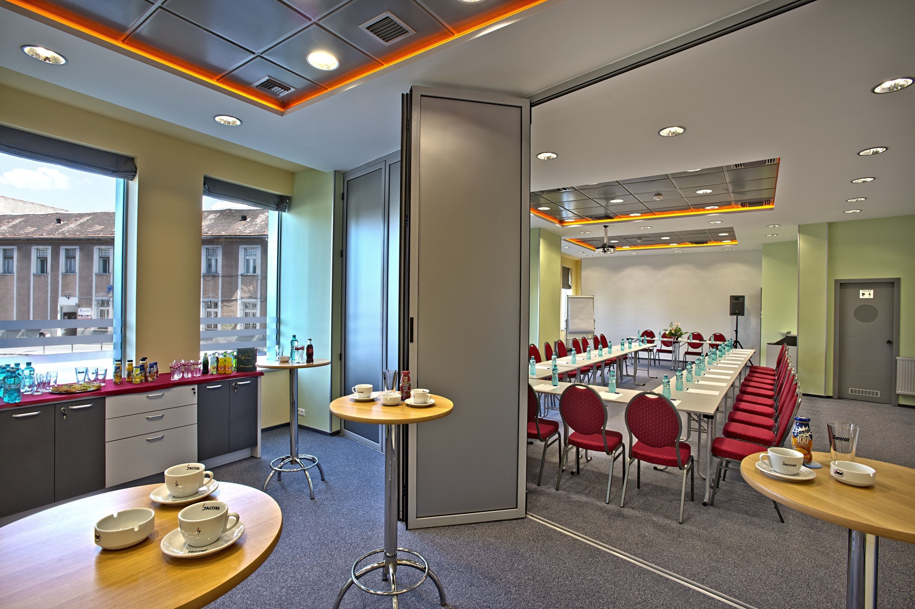 A modern conference room with a long table, red chairs, and a small round table with cups and saucers.