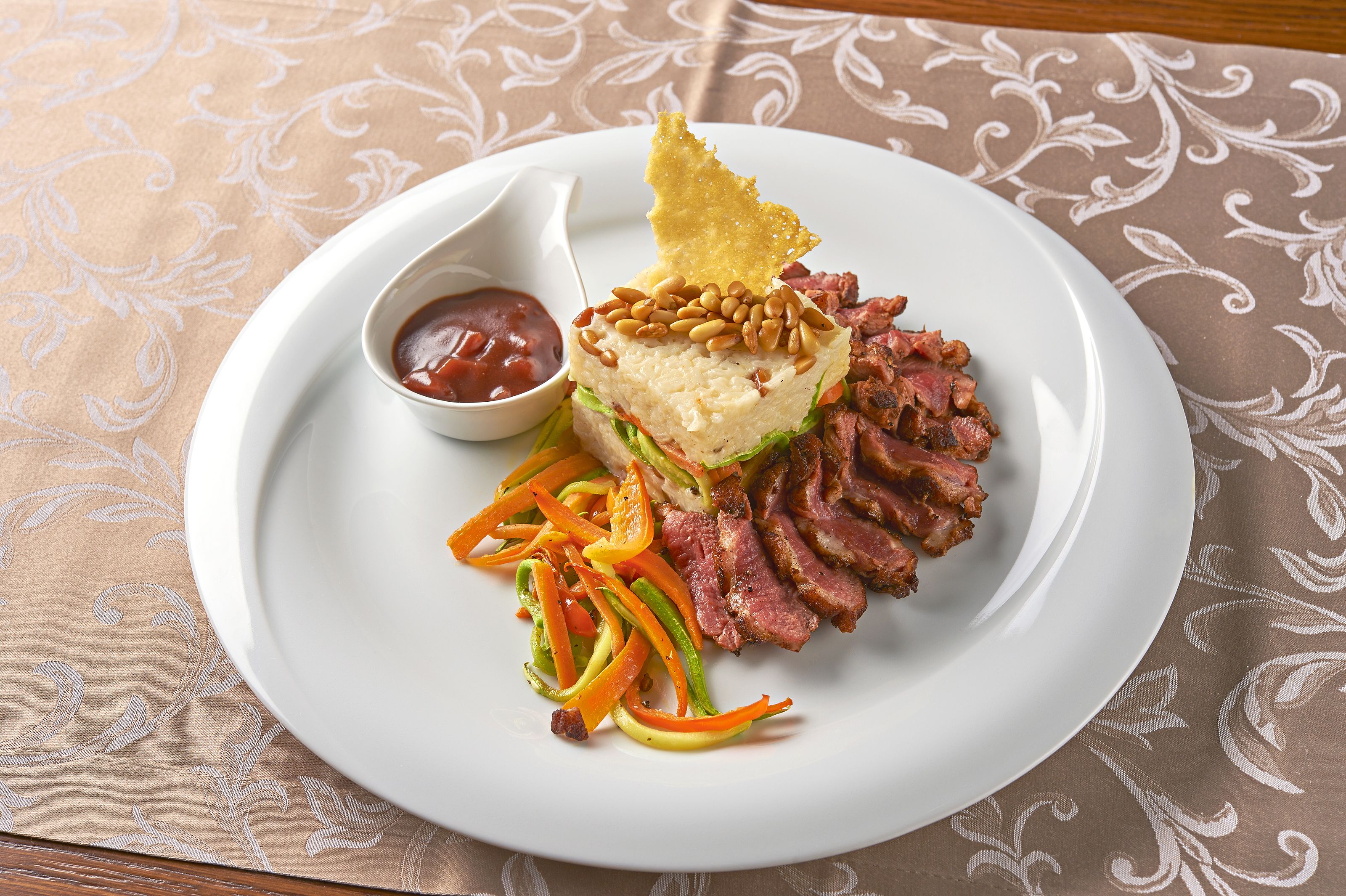 A plate with sliced meat, a dollop of sauce, and a side of vegetables.