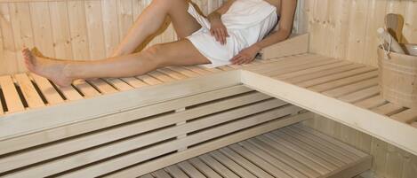 Un sauna en bois, avec une personne allongée sur un banc, une horloge au mur et un banc en bois avec une serviette.