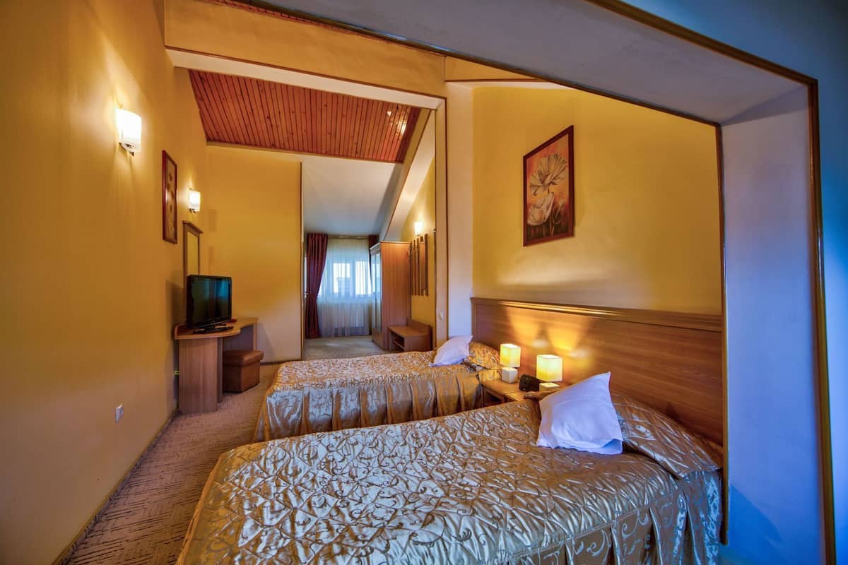 A hotel room with two beds, a television, a desk, and a painting on the wall.