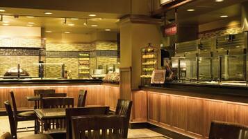 A restaurant with a counter displaying various fruits, wooden chairs, and a brick wall.