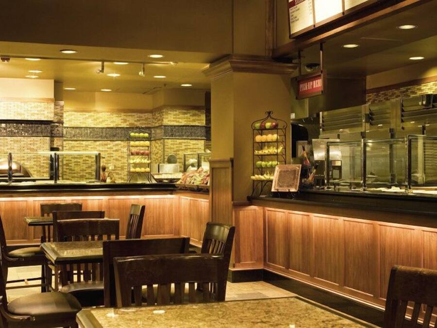 A restaurant with a counter displaying various fruits, wooden chairs, and a brick wall.