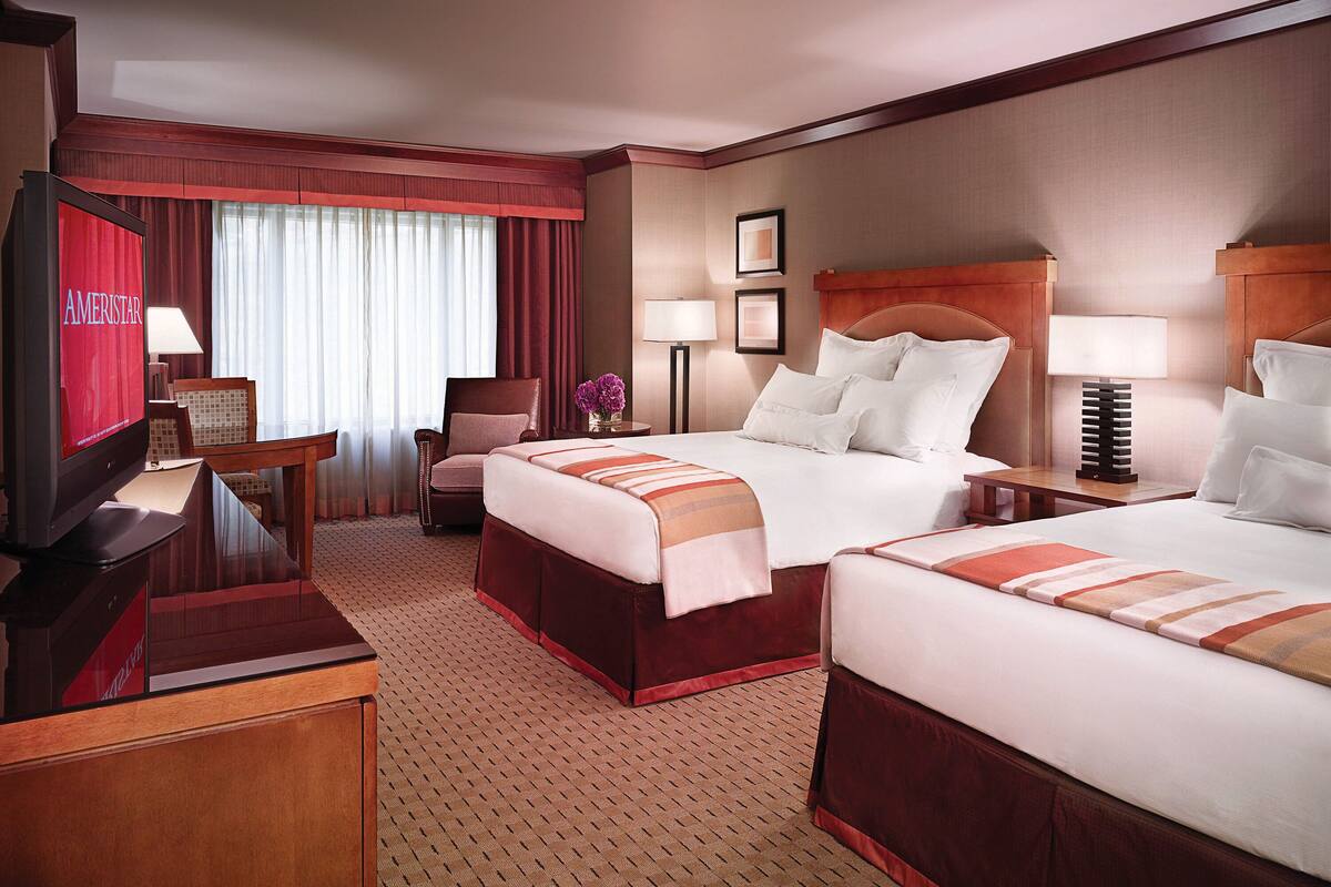 A hotel room with two beds, a desk, a chair, a TV, and a window with curtains.