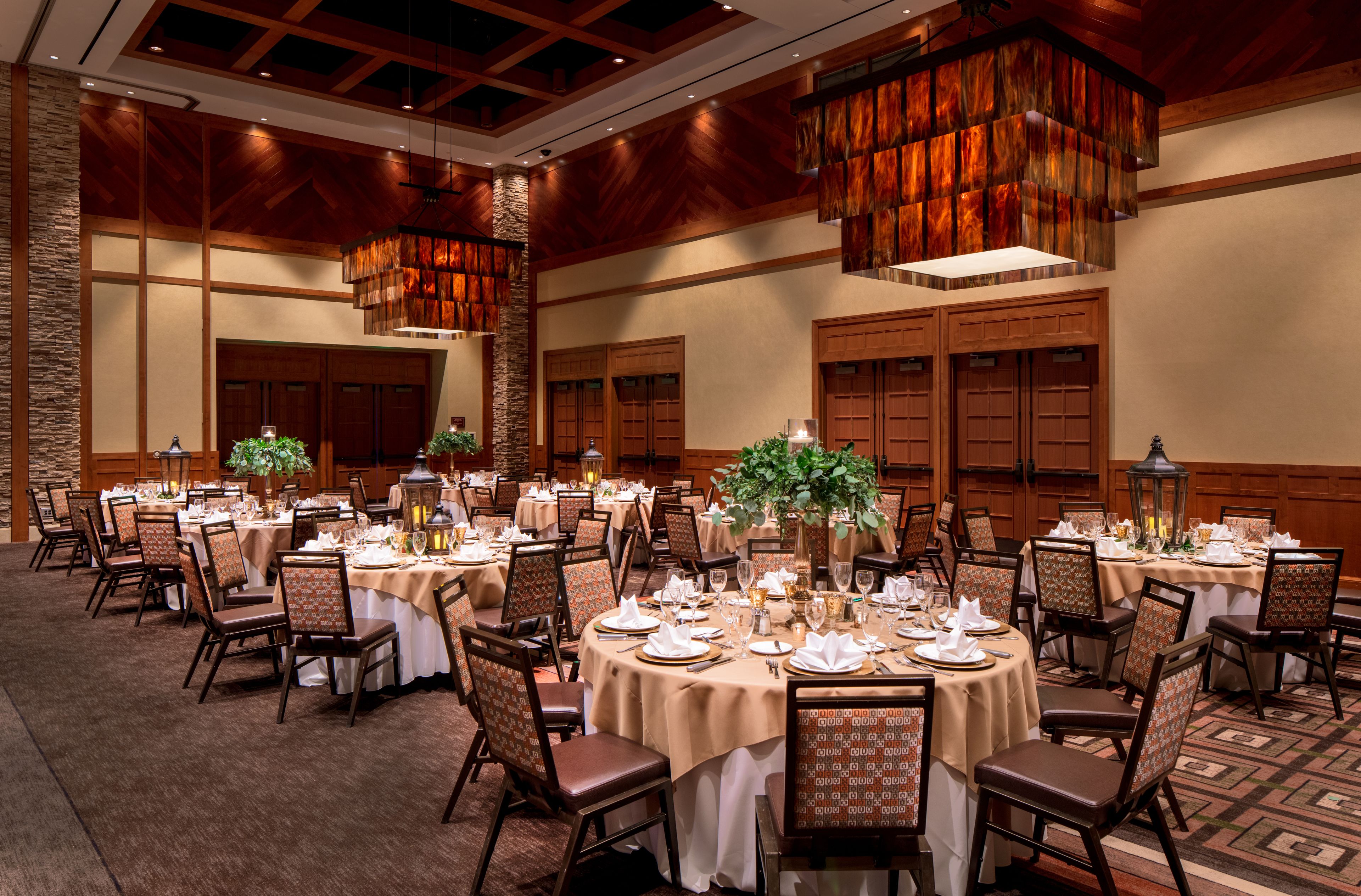 Un salón de banquetes con mesas redondas dispuestas para comer, paneles de madera y candelabros colgantes.