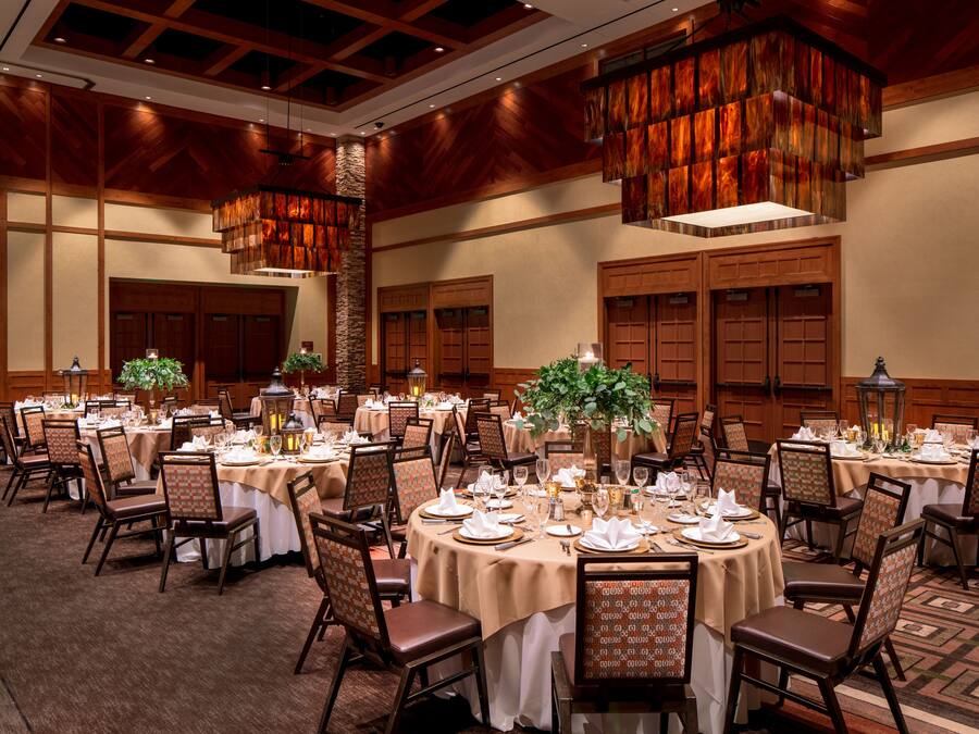 Une salle de banquet avec des tables rondes dressées pour le repas, des boiseries et des lustres suspendus.