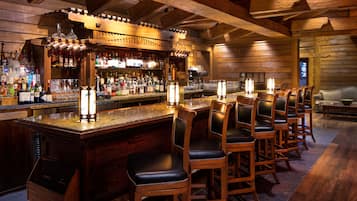 A bar area with wooden bar stools, a bar counter, and a variety of liquor bottles.