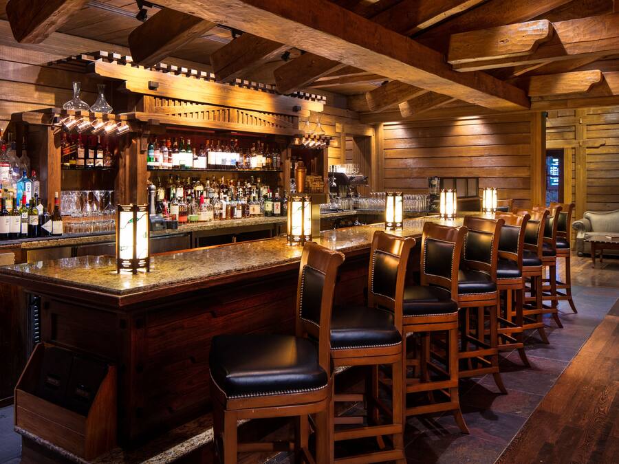 A bar area with wooden bar stools, a bar counter, and a variety of liquor bottles.