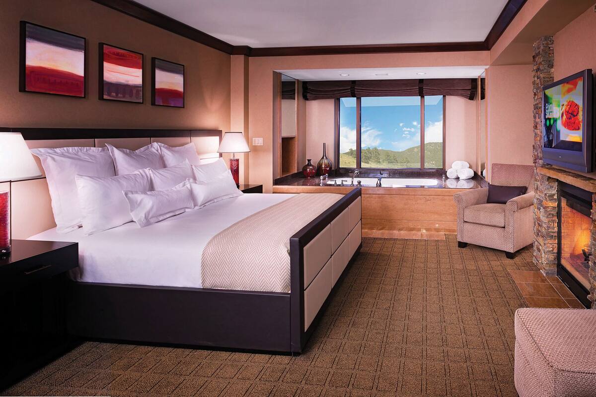 A spacious bedroom with a large bed, a sitting area with a fireplace, and a view of the outdoors.