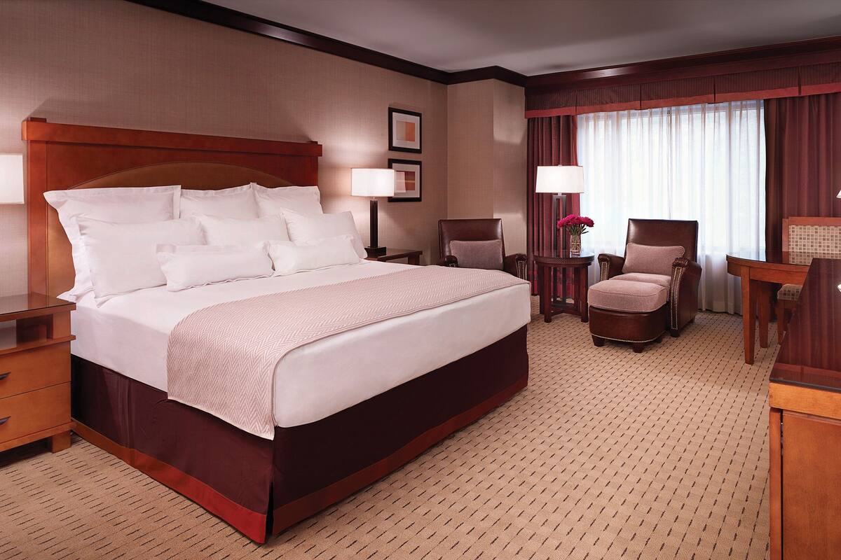 A hotel room with a large bed, a television, a desk with a lamp, and a chair.