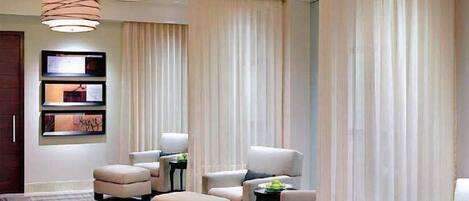 A modern hotel room with a large seating area, multiple armchairs, a sofa, and a small table with a bowl of fruit.