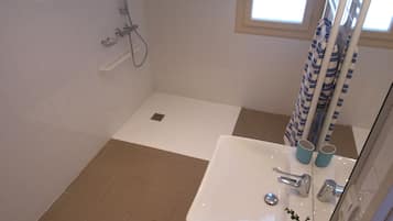 A bathroom with a shower, a sink, and a window.