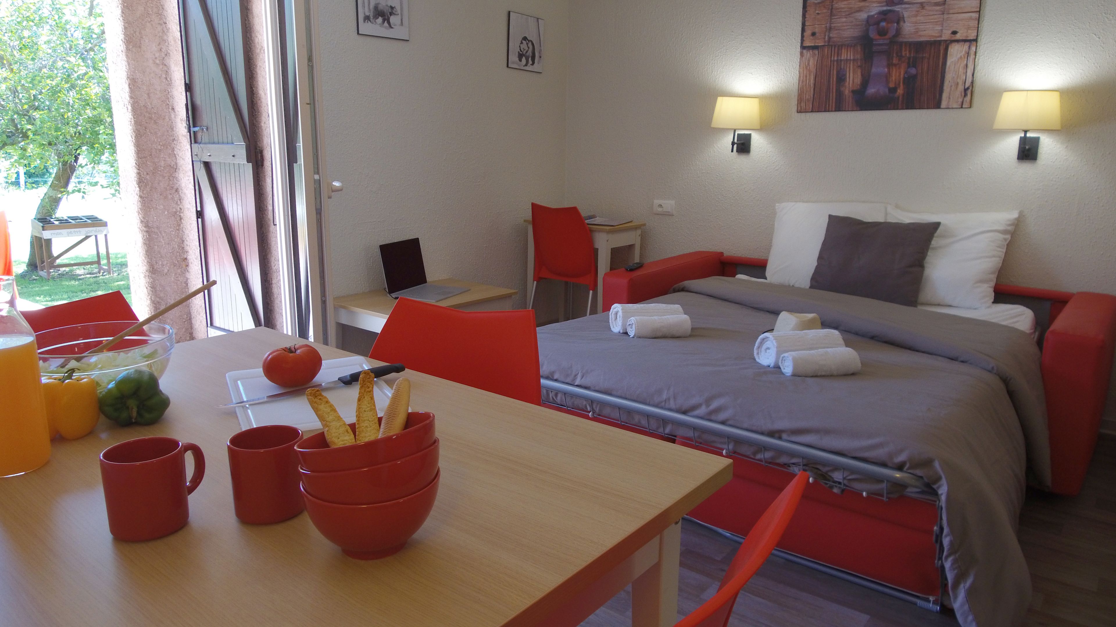 A hotel room with a bed, a table with breakfast items, a laptop, and a window with curtains.