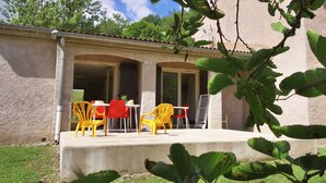 Un área de estar al aire libre techada, con sillas y una mesa de plástico amarillo y rojo, rodeada por una estructura de concreto con techo de baldosas.