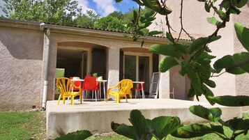 Uma área de estar ao ar livre coberta, com cadeiras e mesa de plástico amarelas e vermelhas, rodeada por uma estrutura de concreto com telhado de azulejos.