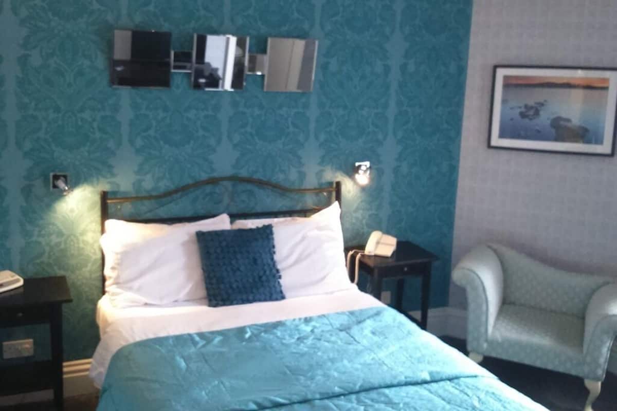 A bed with a blue bedspread, a headboard, and a bedside table with a lamp.
