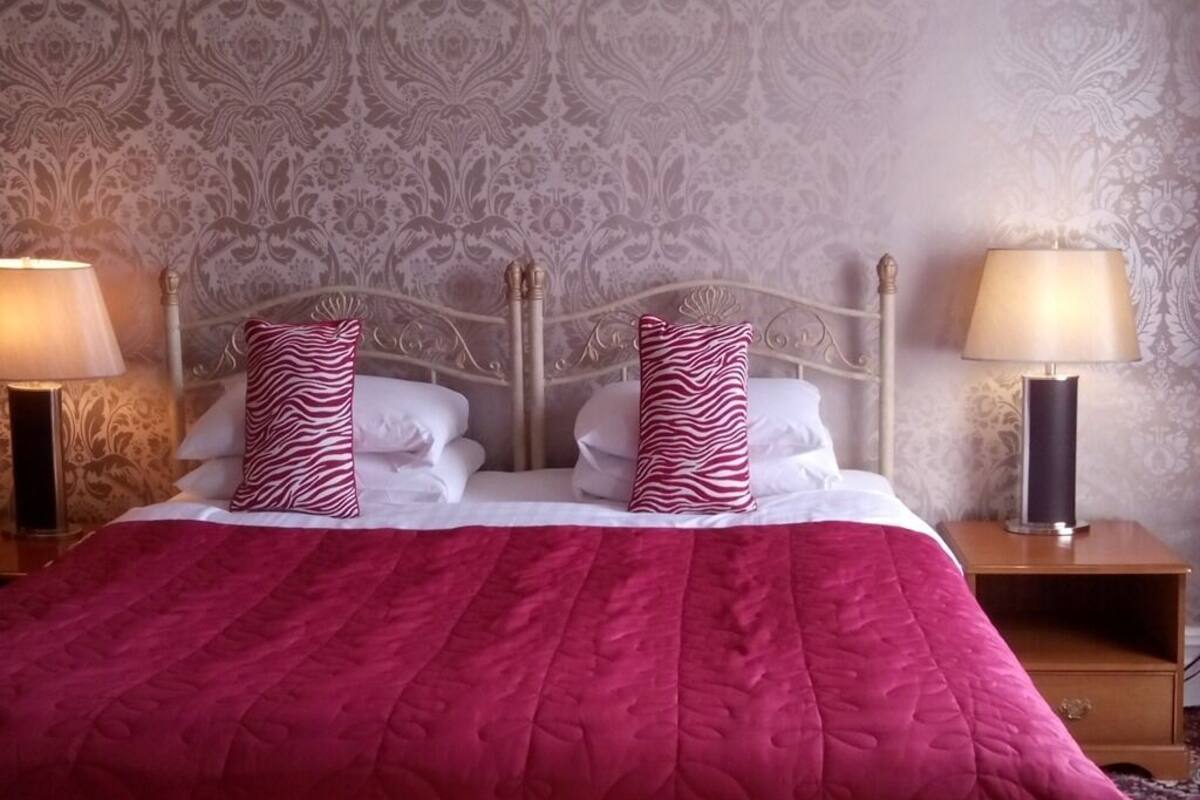 A neatly made bed with a red quilt, two zebra-patterned pillows, and two white pillows. There are two bedside tables with lamps, one on each side of the bed.