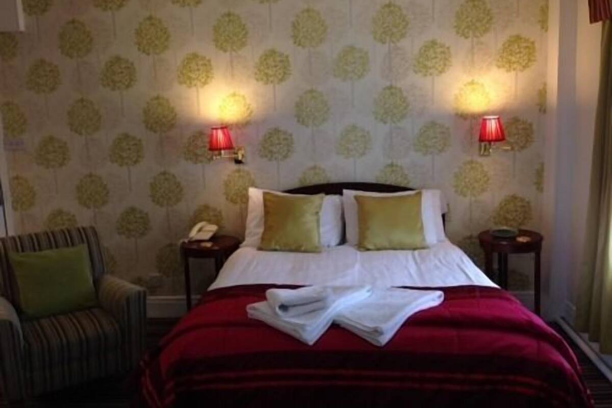 A hotel room with a bed, two bedside lamps, a chair, and a patterned wallpaper.