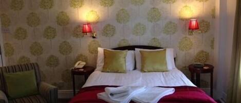 Een hotelkamer met een bed, twee bedlampjes, een stoel en behang met een patroon.