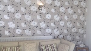 A living room with a beige sofa, patterned cushions, a small wooden side table, and a floral wallpaper. - Hardwicke Hall Manor Hotel (Hartlepool)