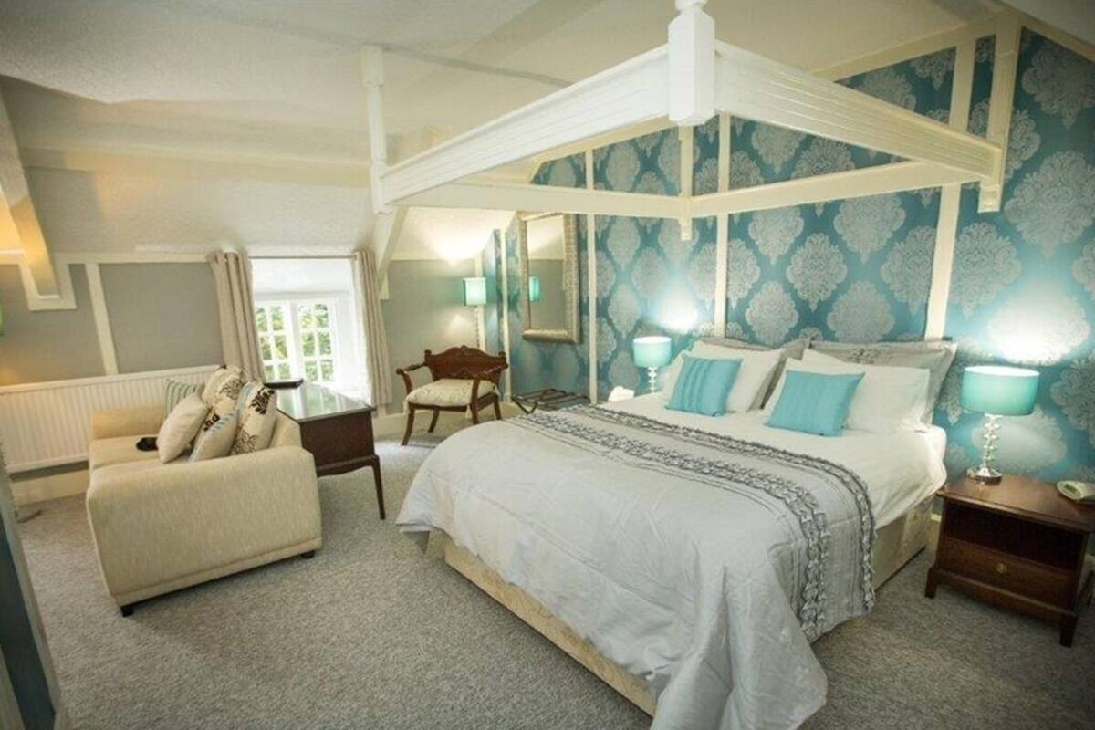 A bedroom with a canopy bed, a sitting area with a sofa, and a chair.