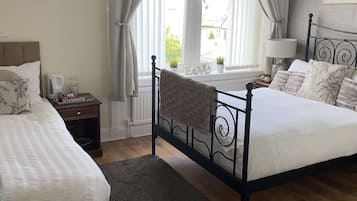 A bedroom with two beds, a window with curtains, a bedside table with a lamp, and a view of the outside.
