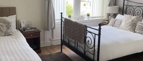 Un dormitorio con dos camas, una ventana con cortinas, una mesita de noche con lámpara y vistas al exterior.