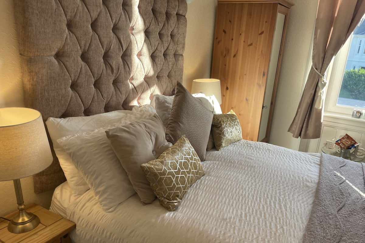 A neatly made bed with a tufted headboard, a bedside table with a lamp, and a wooden wardrobe in a hotel room.