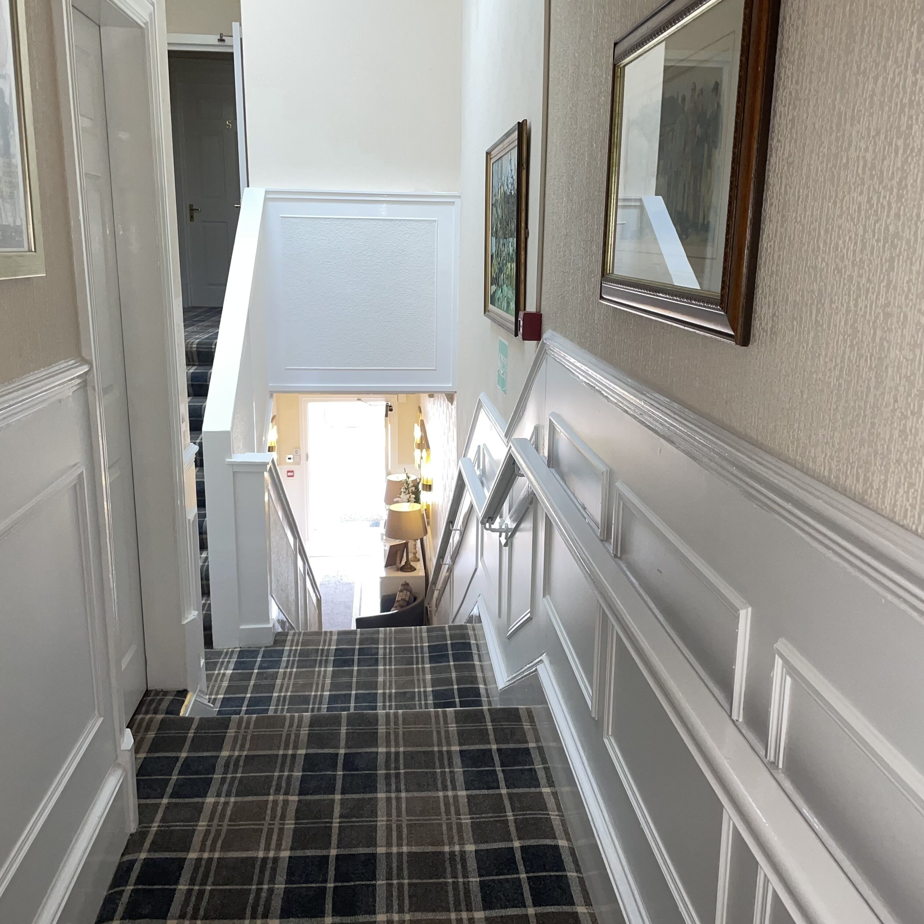A staircase with a plaid carpet leading to a landing area with a lamp and a framed picture.