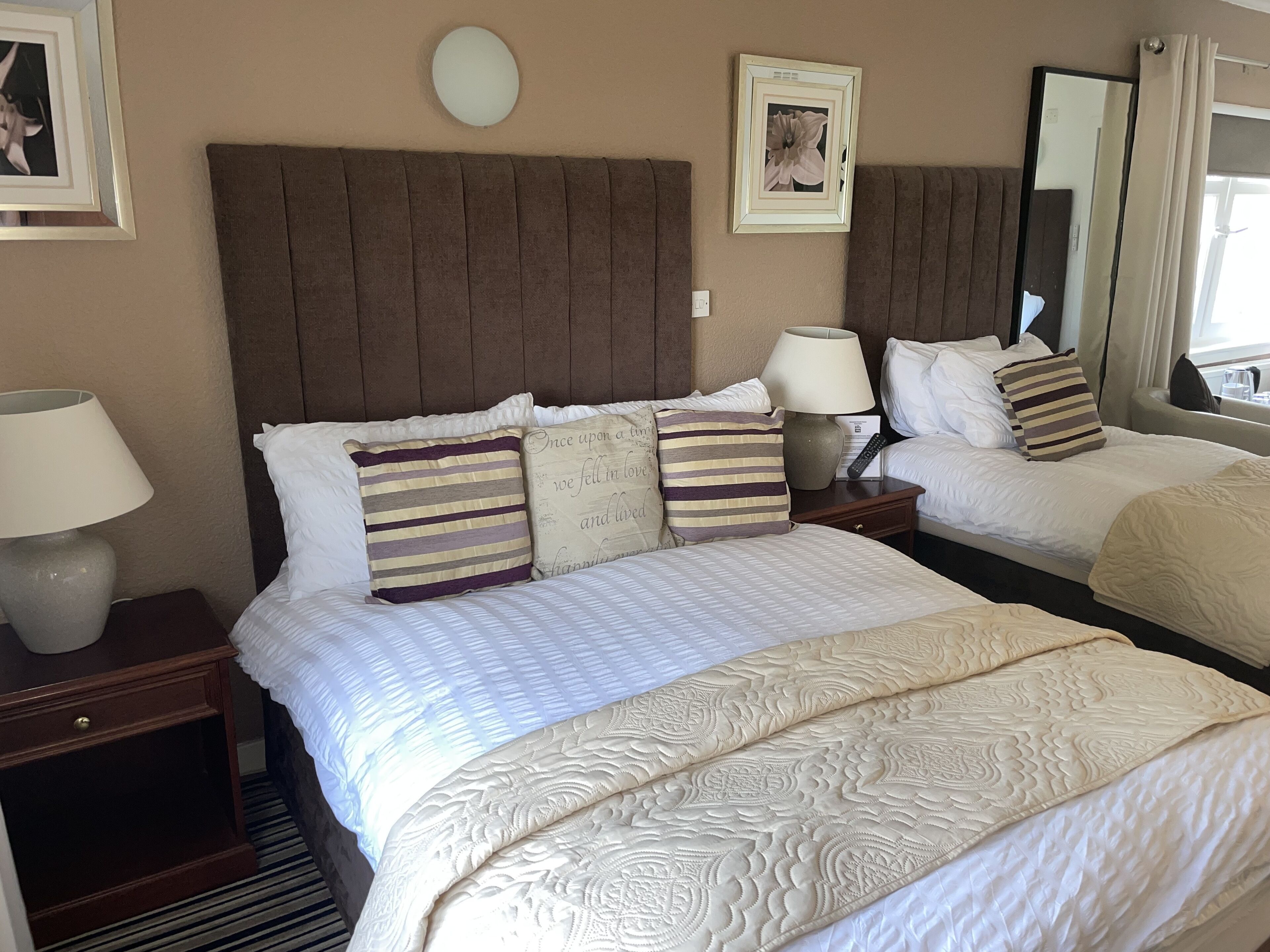 A hotel room with two beds, a nightstand with a lamp, a wall clock, and a framed picture.