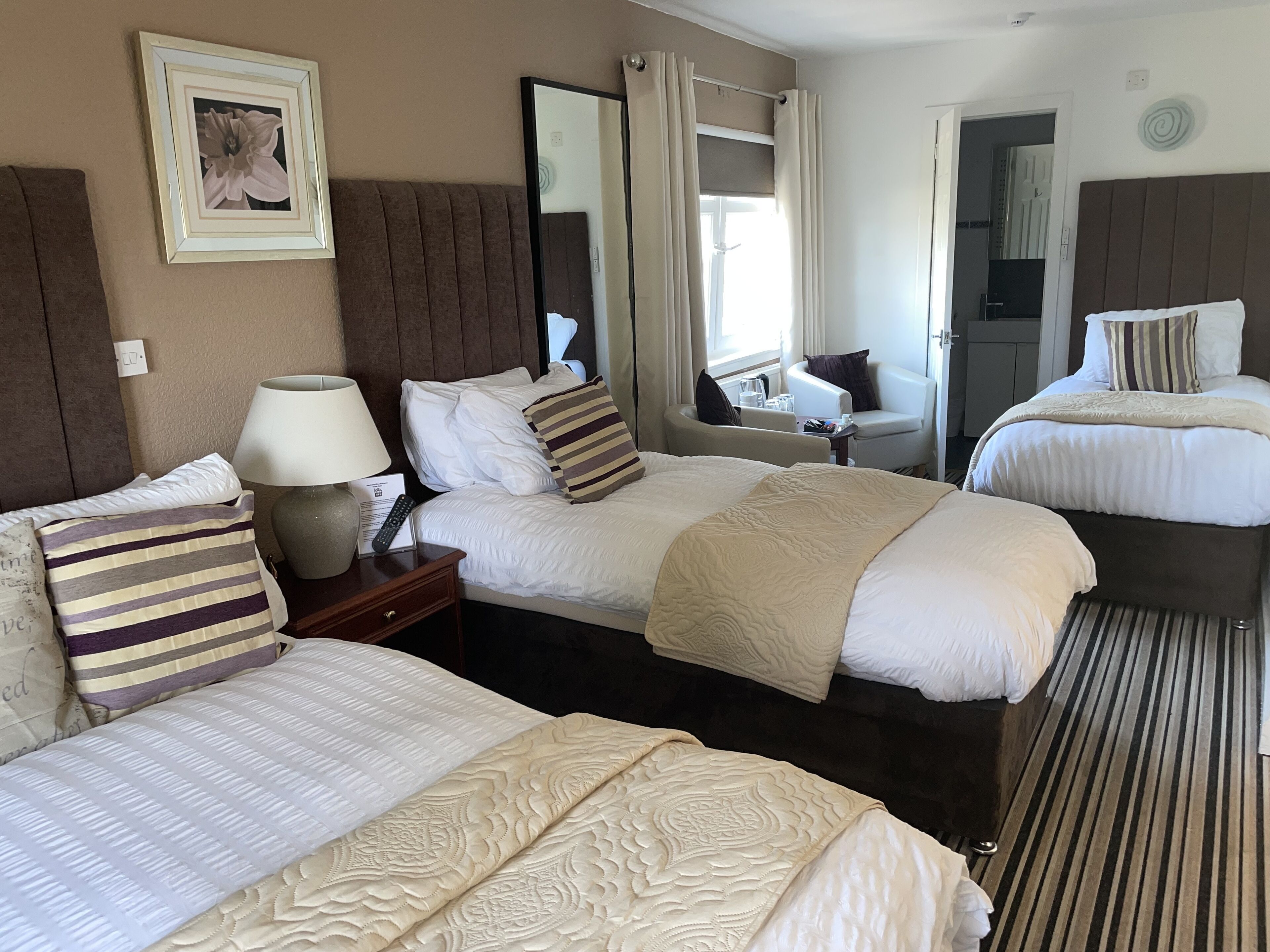 Une chambre d’hôtel avec deux lits, un coin salon, un miroir et une fenêtre avec des rideaux.