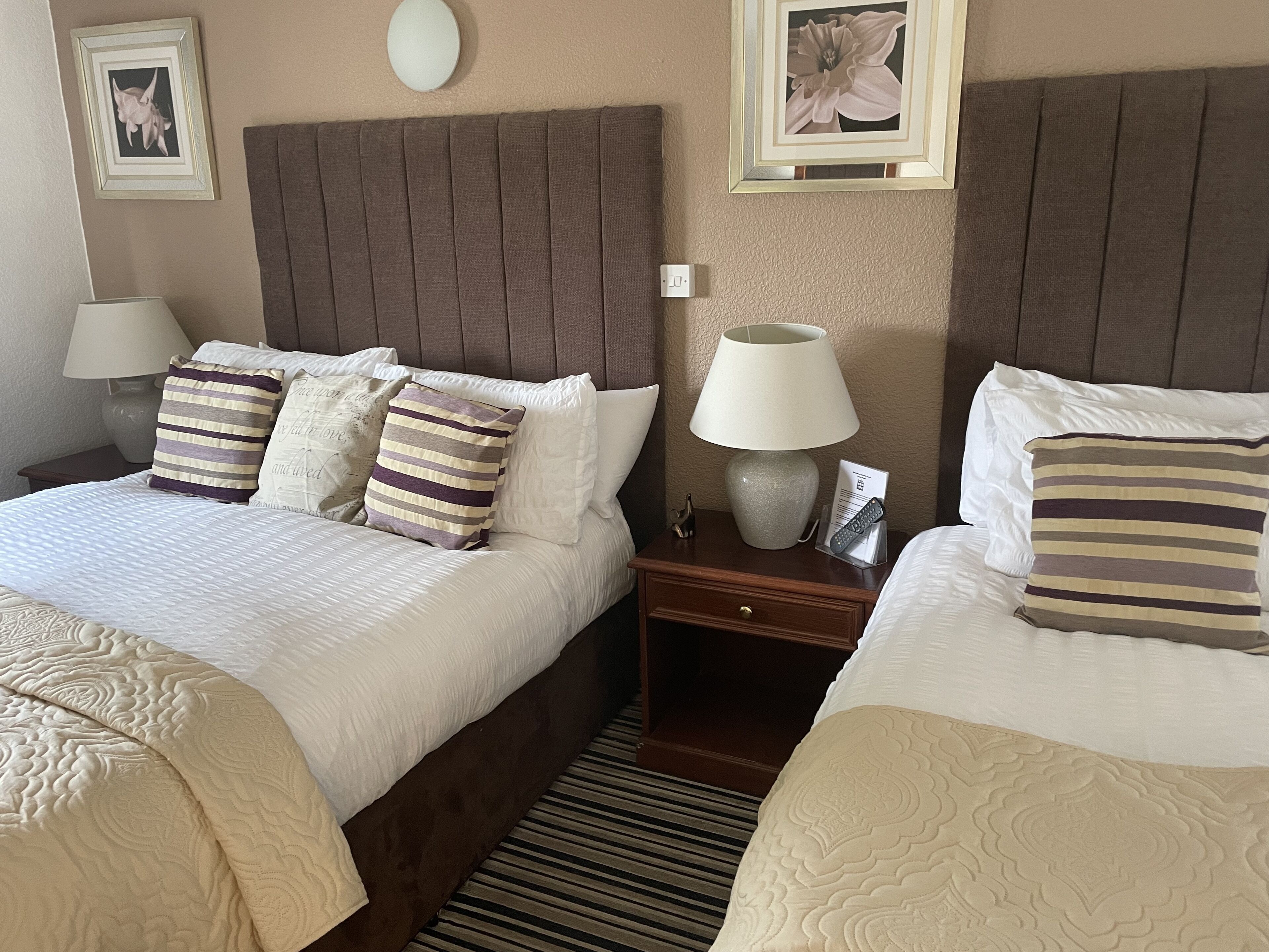 A hotel room with two beds, each with a headboard, bedside tables, lamps, and decorative pillows.
