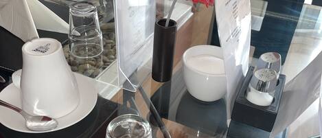 A glass display table with various white ceramic items, including cups and a vase with a red flower.