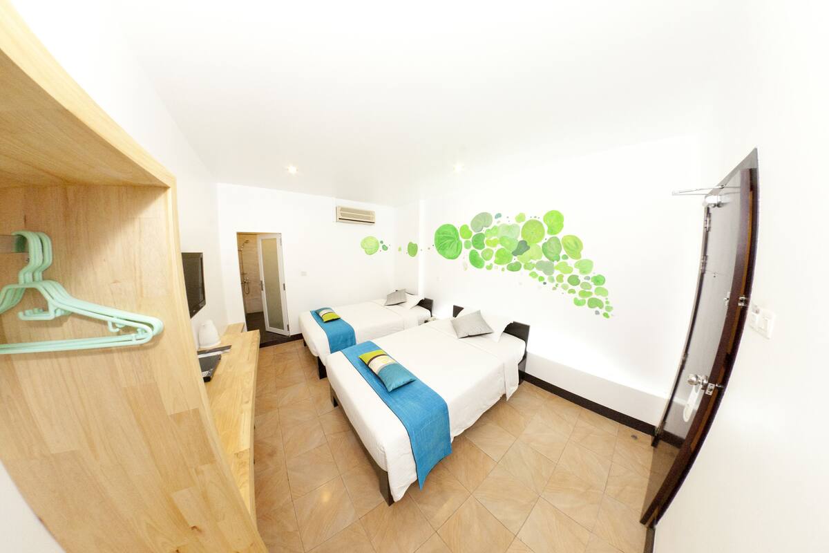 Habitación de hotel con dos camas, un armario de madera, un perchero verde y una decoración en la pared.